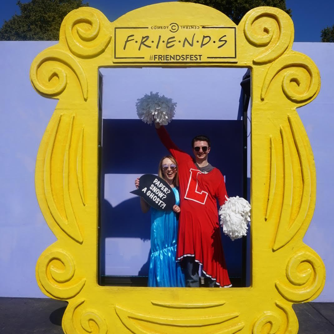 Liam and I stood in the middle of the iconic frame that sits on Monica's door. I'm wearing Rachel's blue prom dress and holding a sign that says "Paper? Snow? A ghost?!" while Liam is wearing Rachel's red cheerleader uniform and cheering with pom-poms.