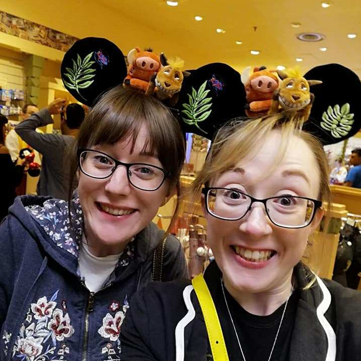 Lillie and I in the hotel gift shop. We're both giving huge grins and wearing Mickey Mouse ears with Timon and Pumbaa on top of them. 
