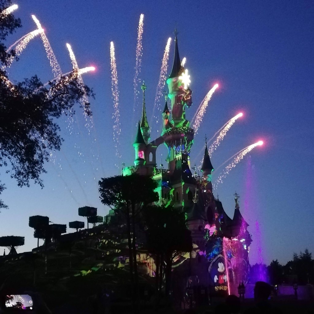 The Disneyland castle lit up and surrounded by fireworks at twilight