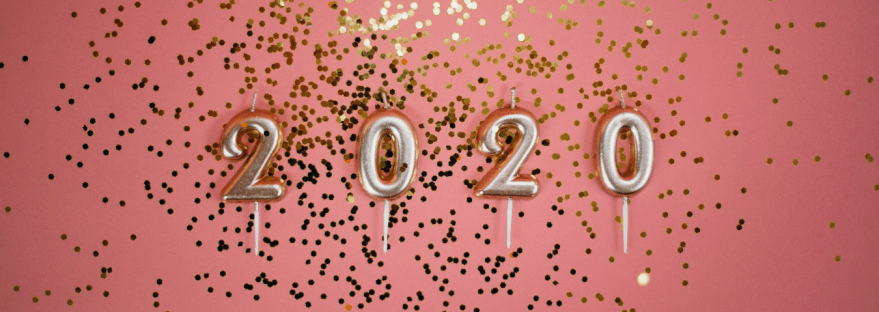 Number candles spelling out 2020 against a pink background with gold confetti