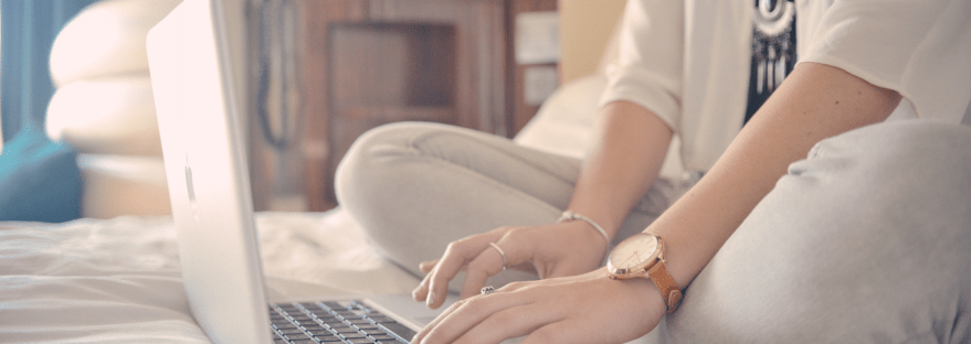 Woman sat on bed typing on a computer
