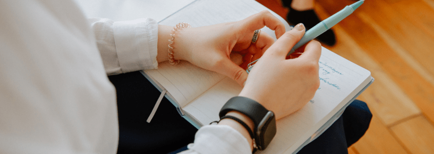 Close up of hands resting on a notebook and holding a pen