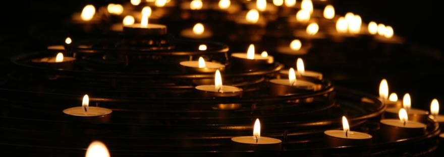 An array of tealights lit up against a dark background